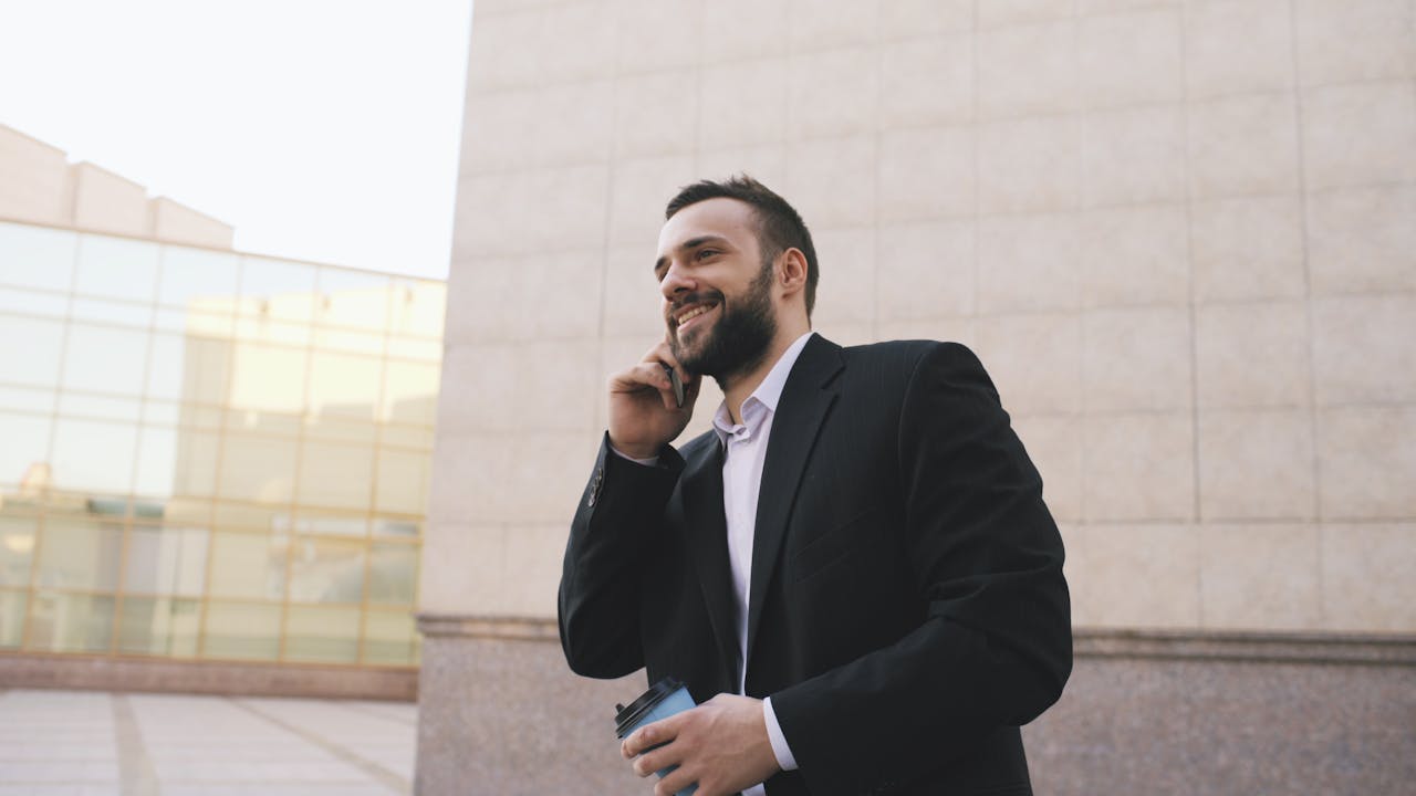 Businessman in suit talking on mobile, holding coffee, urban setting.