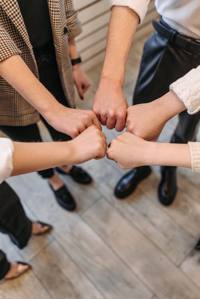 A close-up of five people fist bumping, symbolizing teamwork and unity indoors.